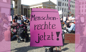 Titelbild: viele Menschen mit Plakaten auf einer Demo, viele sitzen im Rollstuhl, andere stehen oder sitzen auf dem Boden. Im Vordergrund übergroß ein in sehr großer Handschrift beschriebenes Plakat 