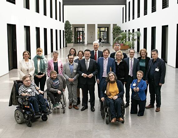 Foto: Gruppenbild mit 18 Menschen hoher Halle des Kleisthauses in Berlin. In der Mitte Minister Hubertus Heil, hinter ihm Staatssekretär Dr. Rolf Schmachtenberg. Links und rechts von ihnen die Beiratsmitglieder, manche mit Rollstuhl oder Blindenstock