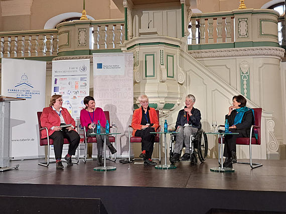 Foto: 5 Teilnehmerinnen sitzen in Schwingsesseln bzw. im Rollstuhl auf dem Podium. Direkt im Hintergrund eine Kirchenkanzel aus Holz, mit Aufgang und angeschlossener Empore